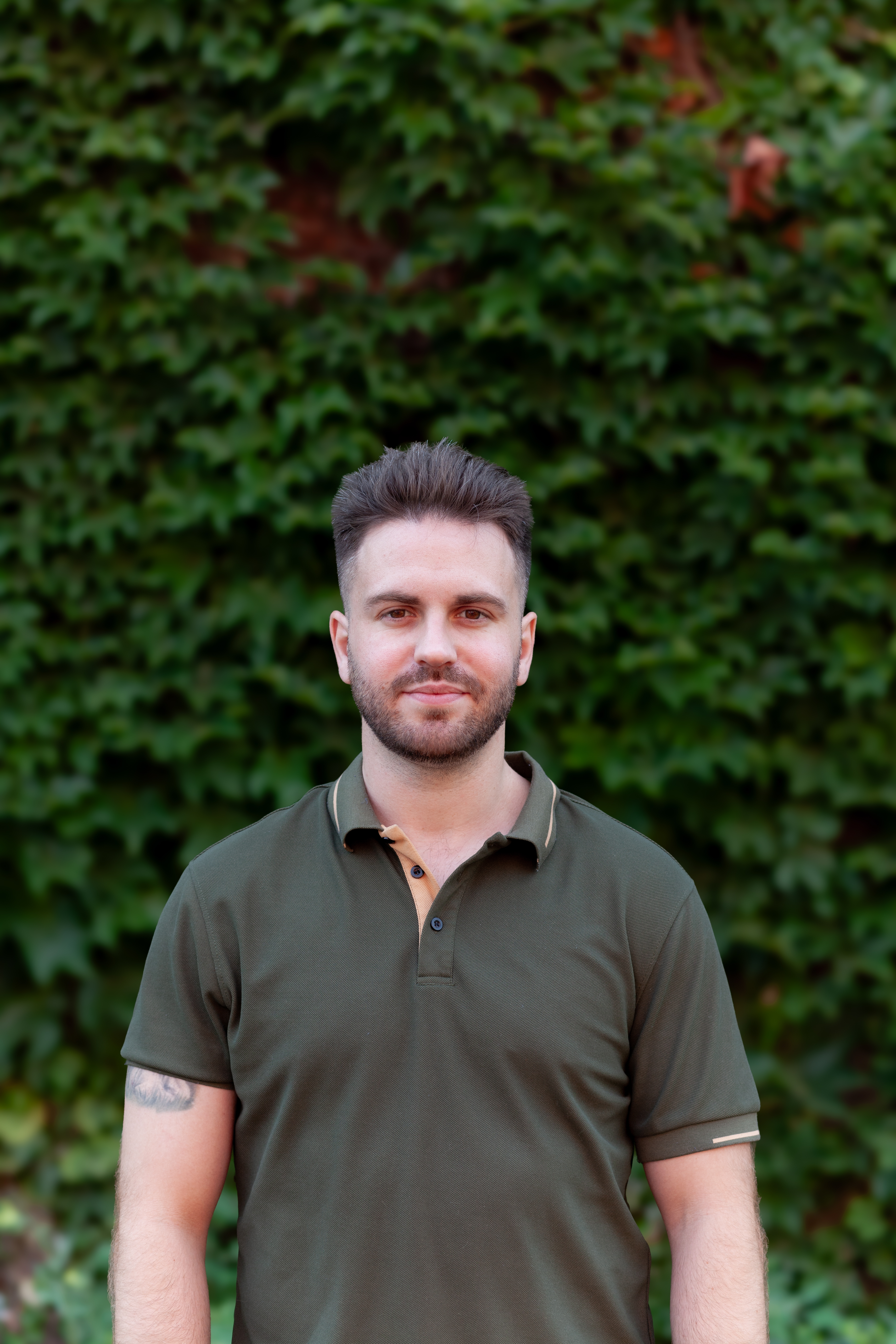 Alex Land in a green polo, in front of ivy